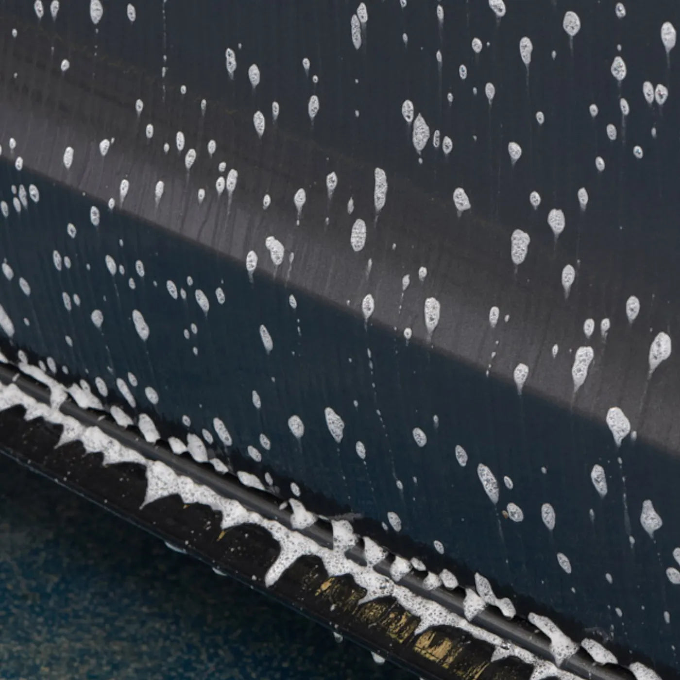 Close-up of a car's black surface with white water droplets on a dark background being cleaned by Advanced TFR by Autoglym
