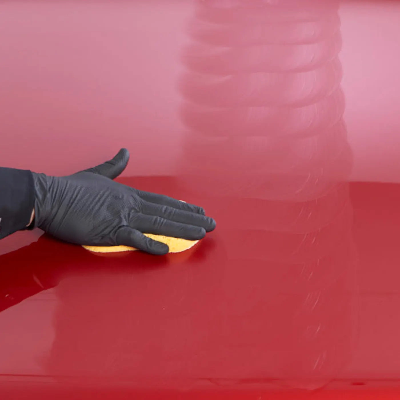 Hand wearing a black glove holding a yellow sponge against a red surface