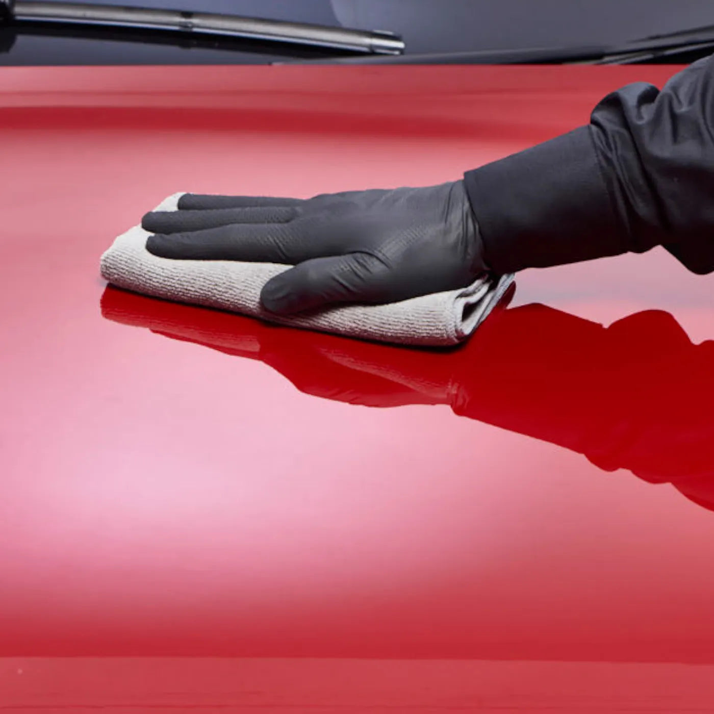 Person cleaning a red car with a cloth and black glove