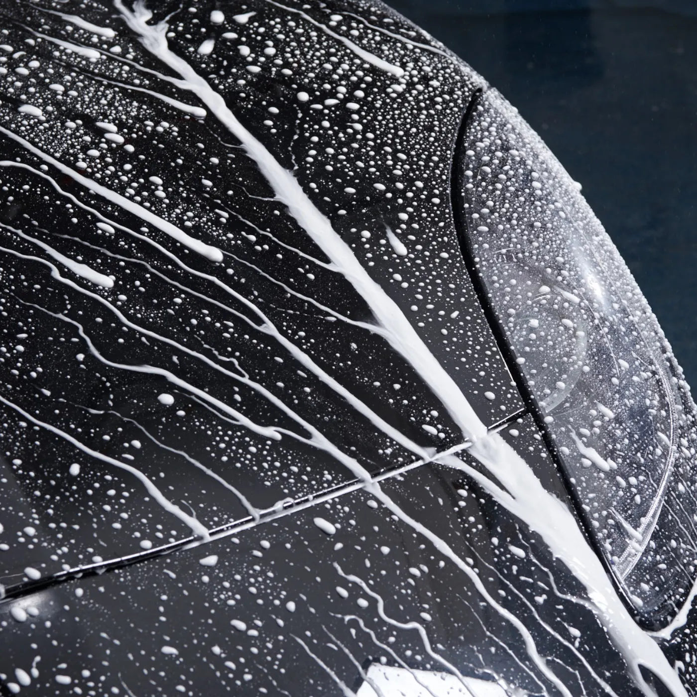 Close-up of a car's black surface with white soap suds