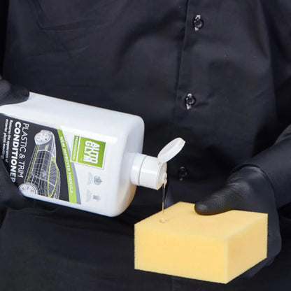 Person holding a bottle of plastic and trim conditioner and a yellow sponge against a black background