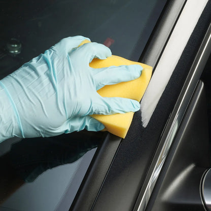 Hand wearing a blue glove cleaning a car window with a yellow sponge.