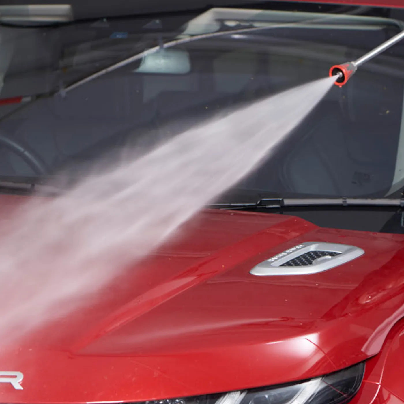 Red car being washed with a high-pressure water gun