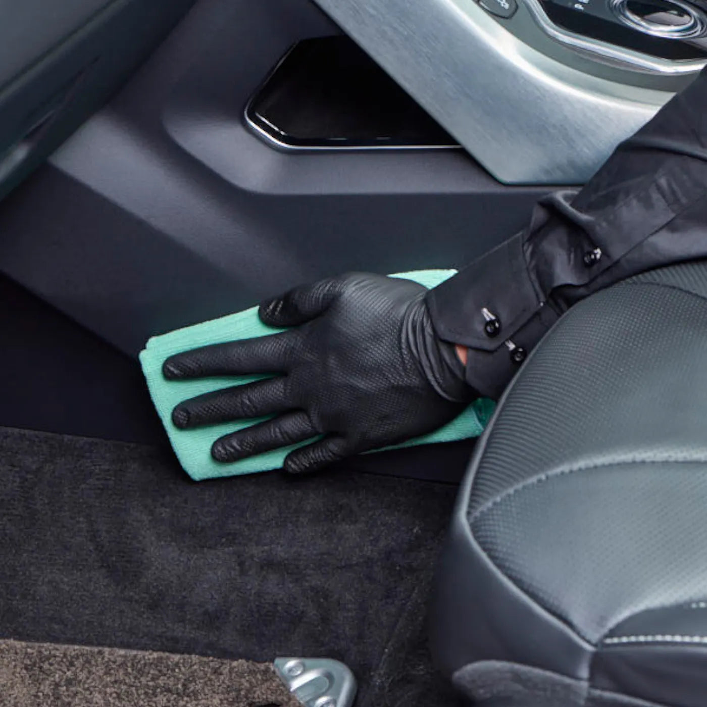 Person cleaning car interior with a green cloth and black gloves