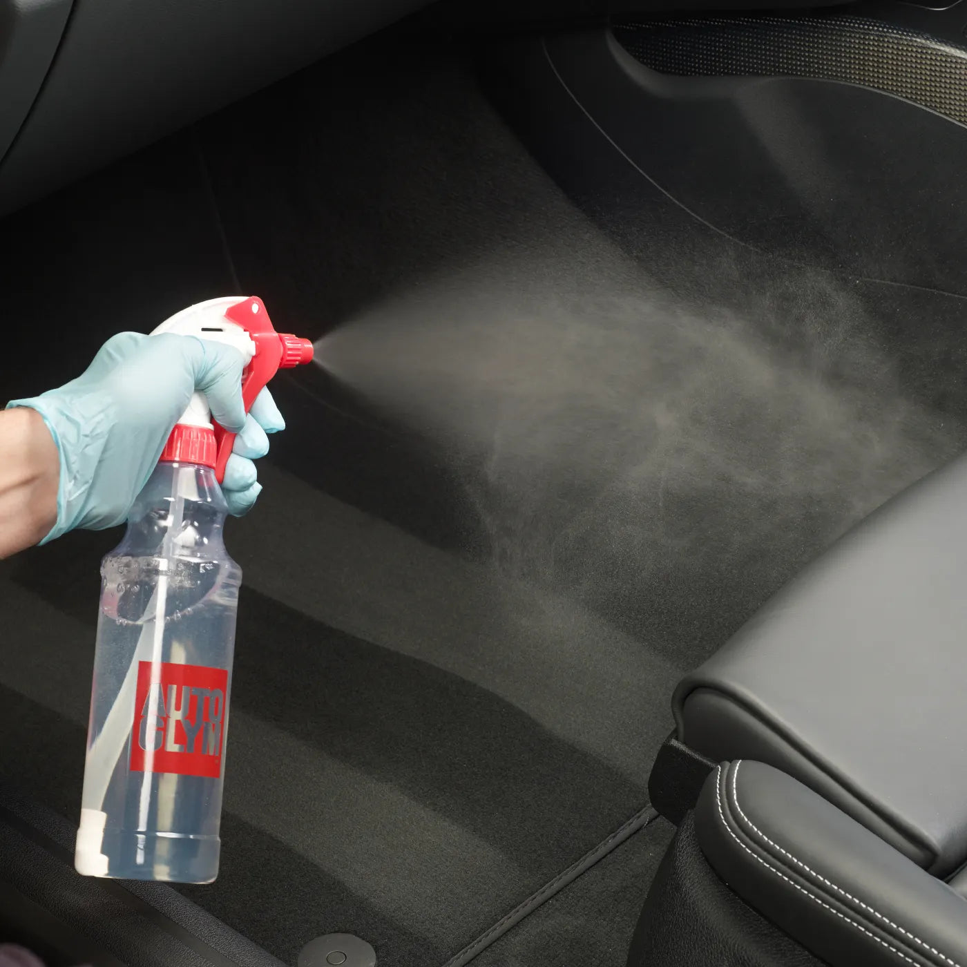Person cleaning car interior with a spray bottle labeled 'DEET'.