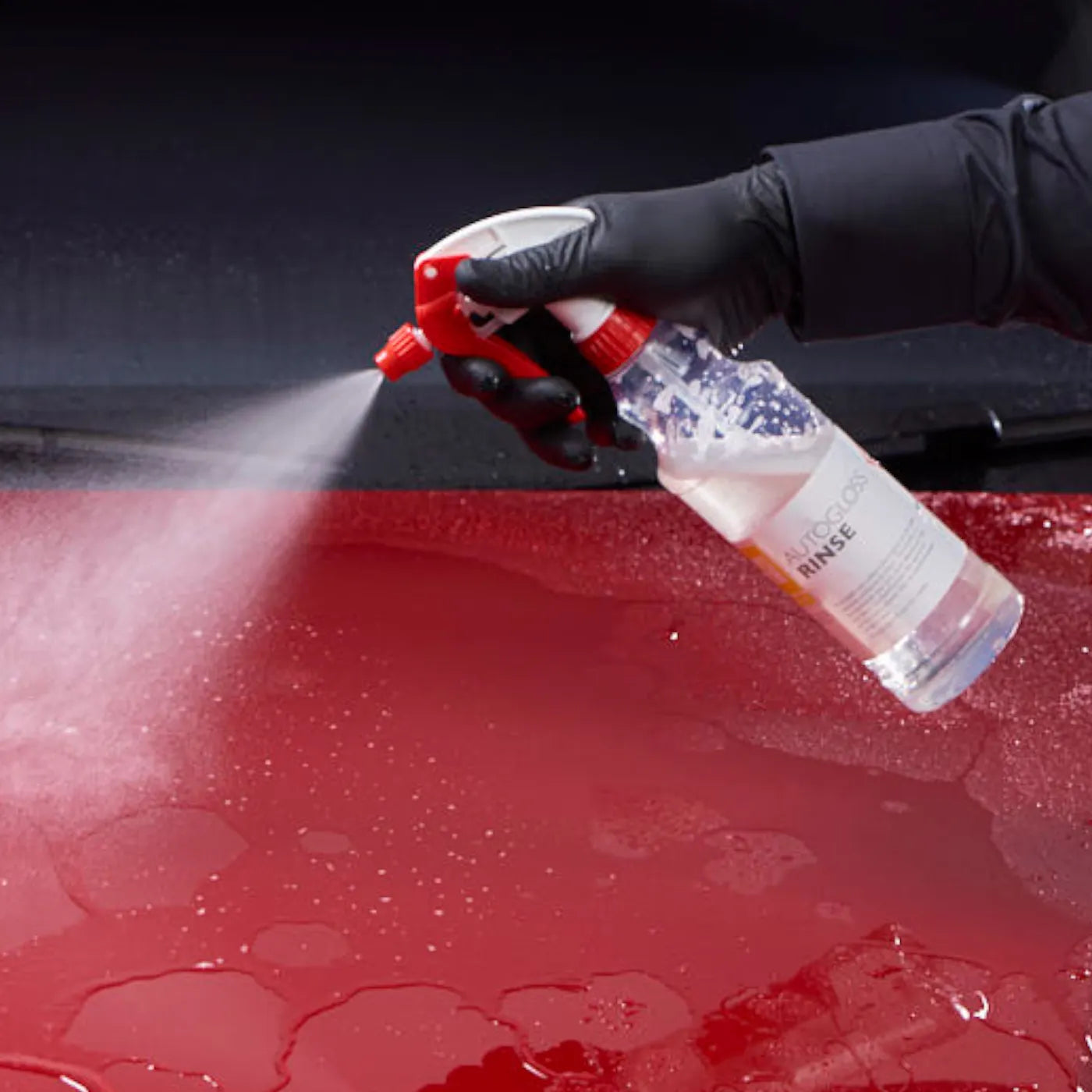 Person using a spray bottle to rinse a red car surface with water.