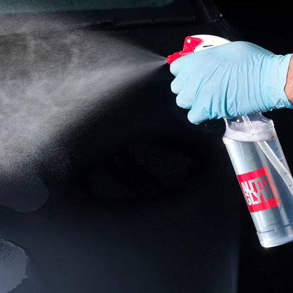 Person wearing a blue glove using a spray bottle labeled 'Clerk' on a dark surface.