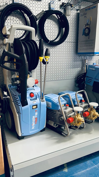 Pressure washer with hoses and nozzles on a shelf in a workshop setting.