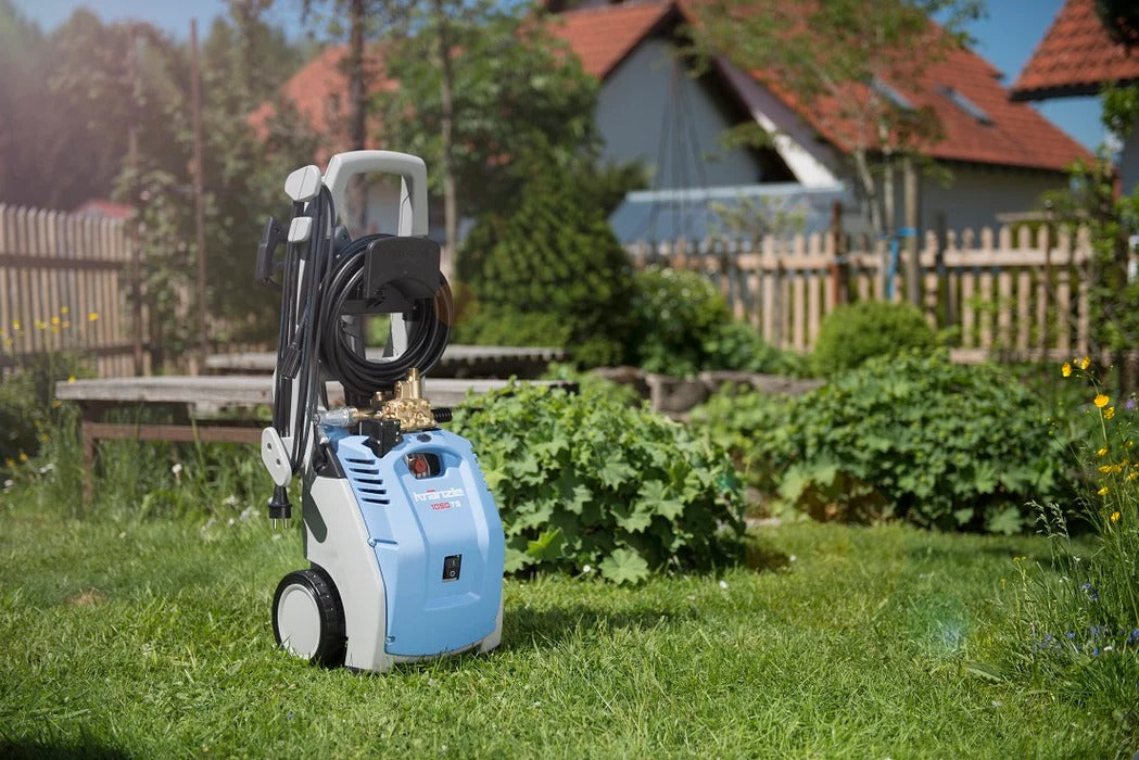 Blue and white pressure washer on grass with garden and houses in the background
