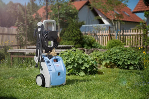 Blue and white pressure washer on grass with garden and houses in the background
