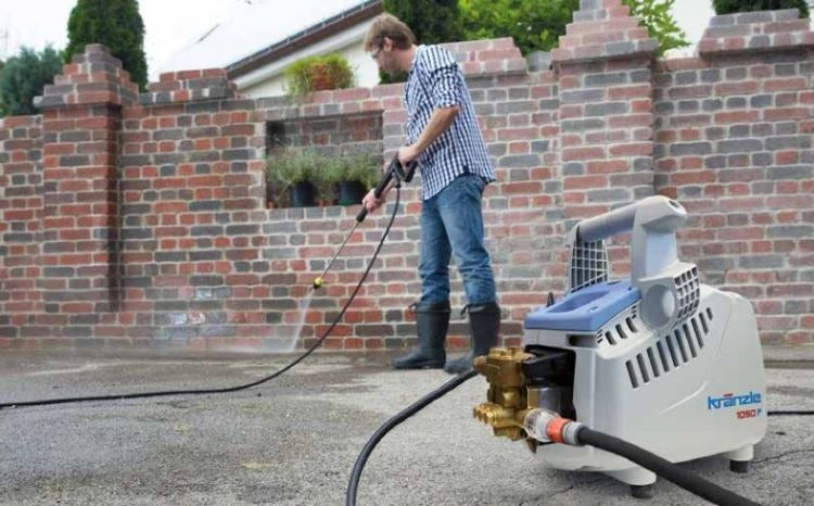 Person using a pressure washer to clean a brick wall