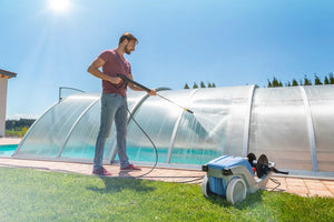Person using a pressure washer to clean a pool area with a clear blue sky.